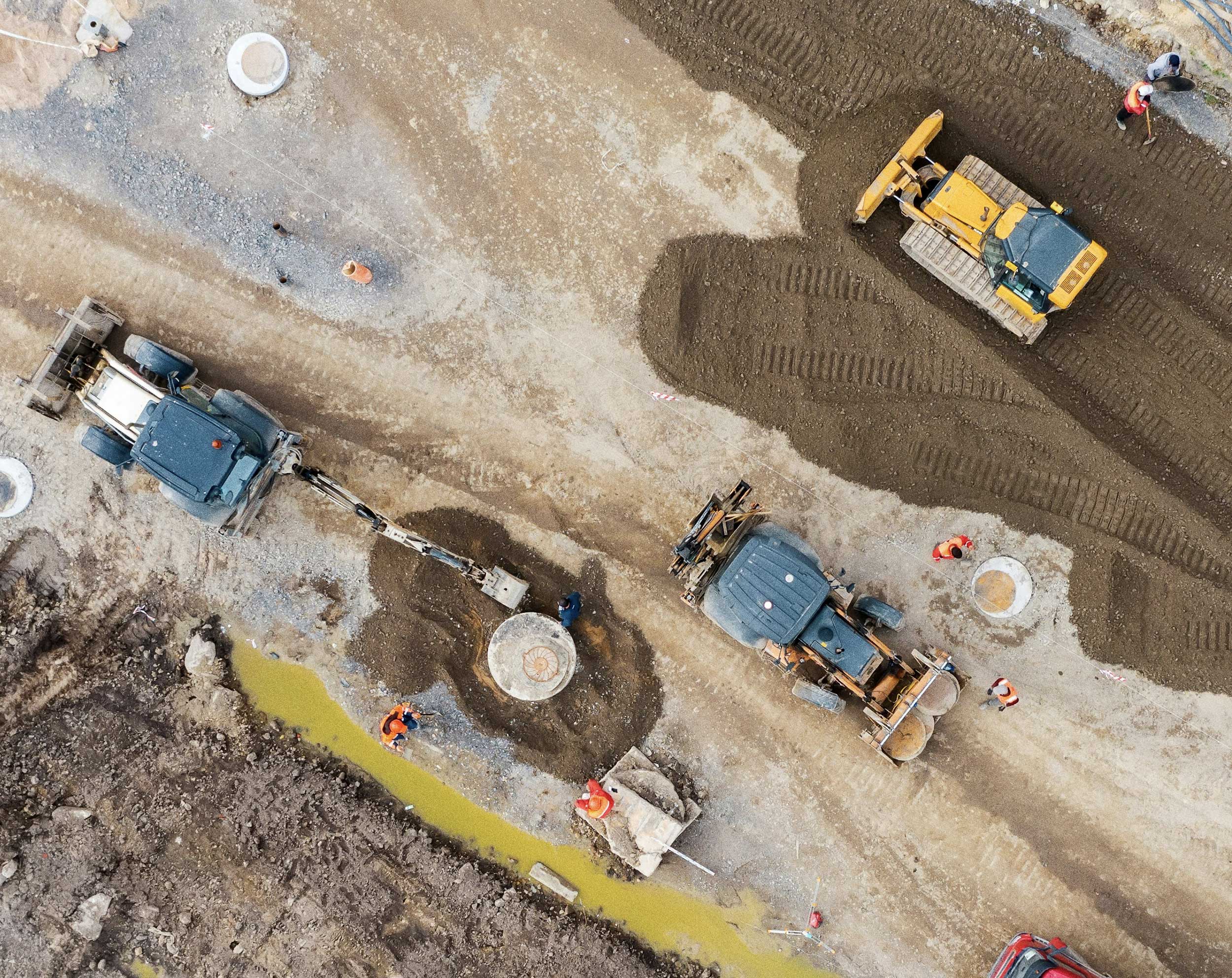 Luchtfoto van bouwvoertuigen en bouwmedewerkers die grondwegen en afwateringszones aanleggen op een bouwterrein.