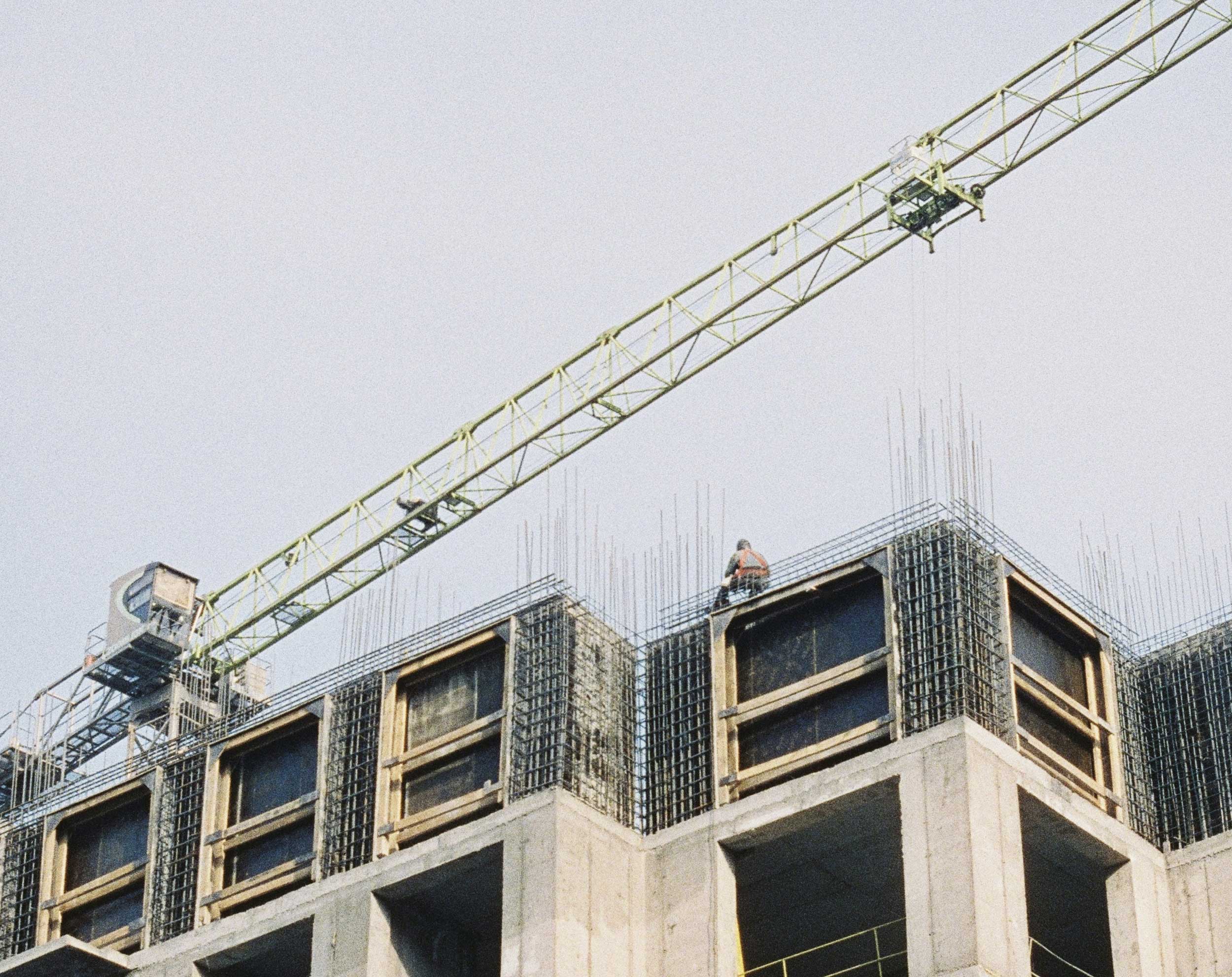 Groene torenkraan boven een onafgewerkt betonnen gebouw met uitstekende wapeningsstaven.