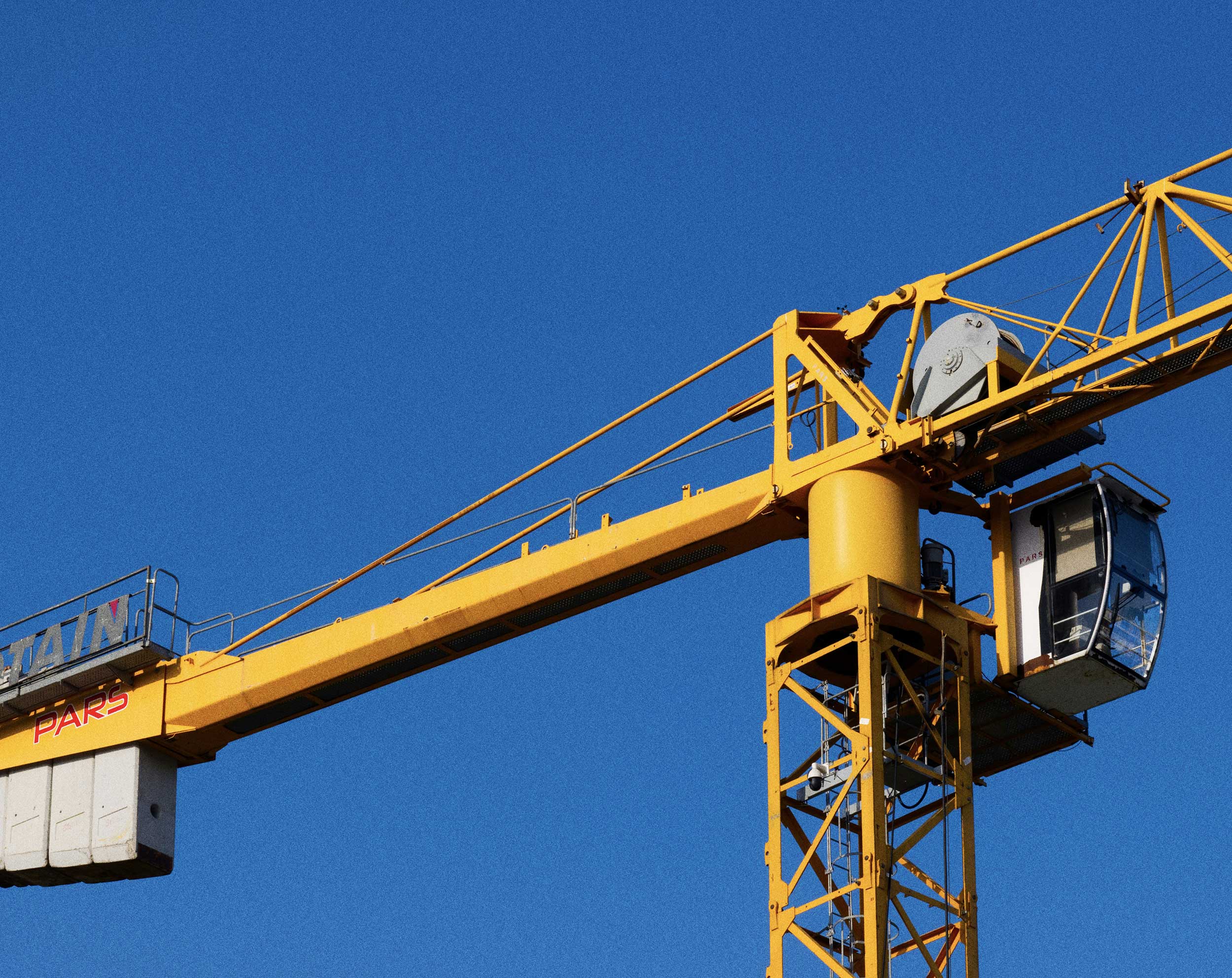 Close-up van een gele torenkraan met machinistencabine tegen een felblauwe lucht.
