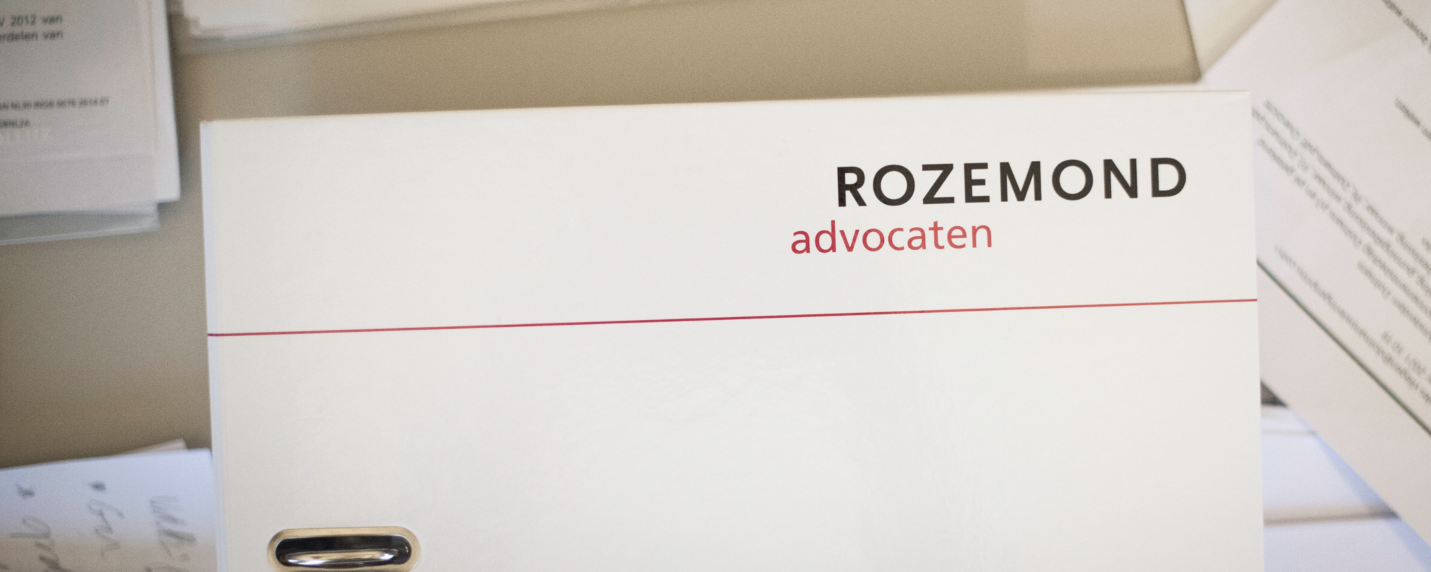Een tafel vol papieren dossiers en een map van Rozemond Advocaten.